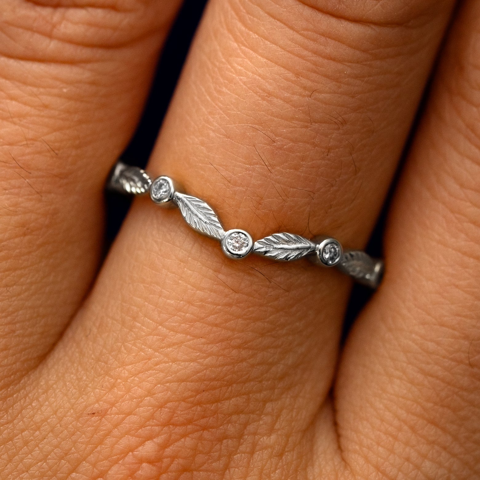 Close up view of a model's fingers wearing a 14k white gold Chevron Leaves and Round Diamonds Band