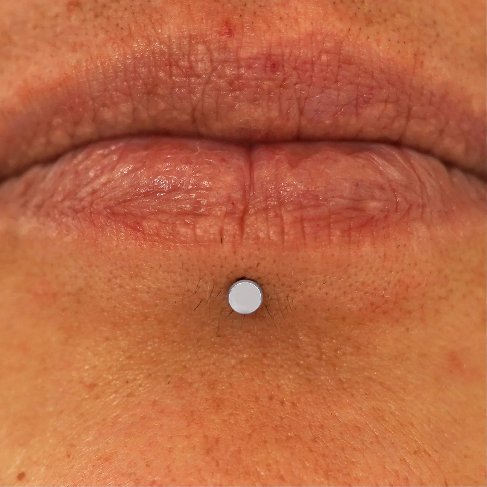Close up view of a model's lips wearing a 14k white gold Mini Circle Flatback in a labret piercing