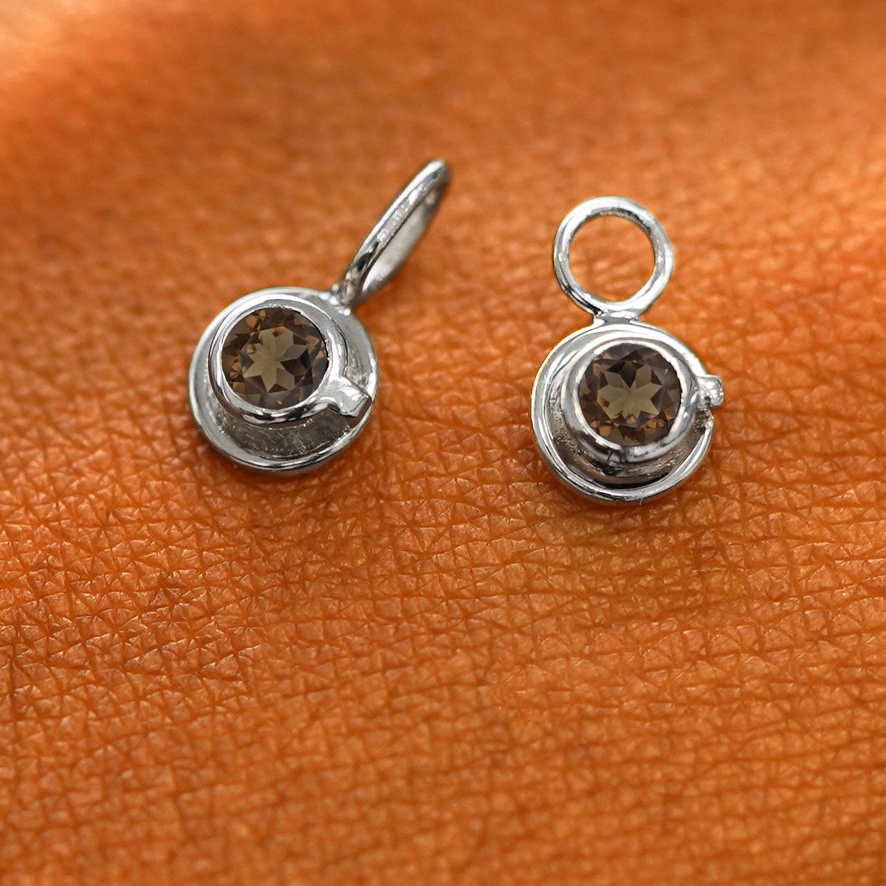 A solid white gold coffee cup charm resting on a back of the model's hand