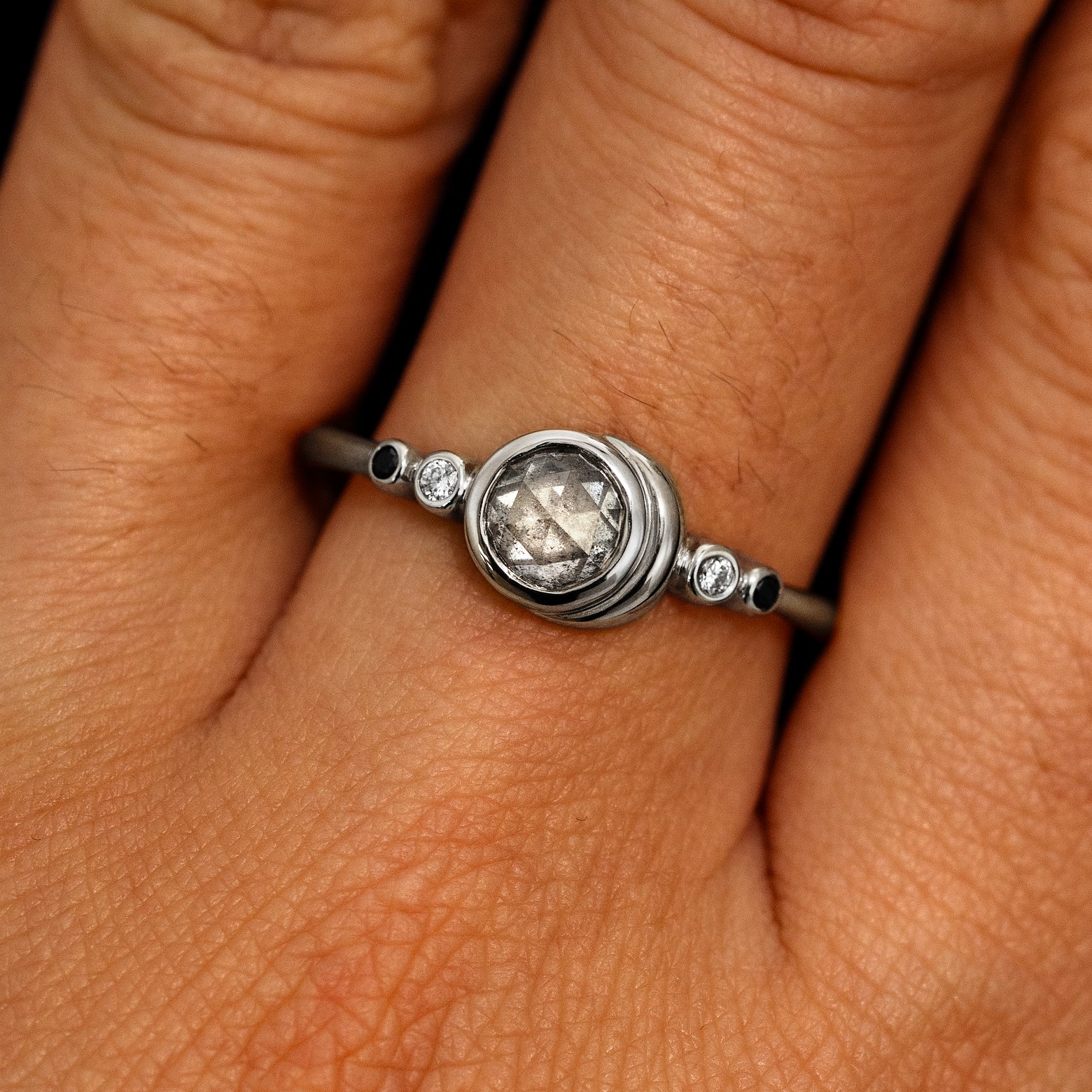 A model's hand wearing a 14k white gold Rose Cut Salt and Pepper Diamond Moon Ring