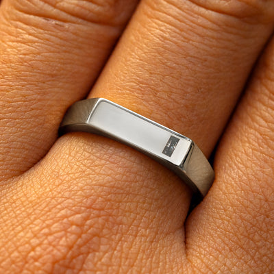 A model's finger wearing a white gold baguette salt and pepper diamond rectangular signet ring