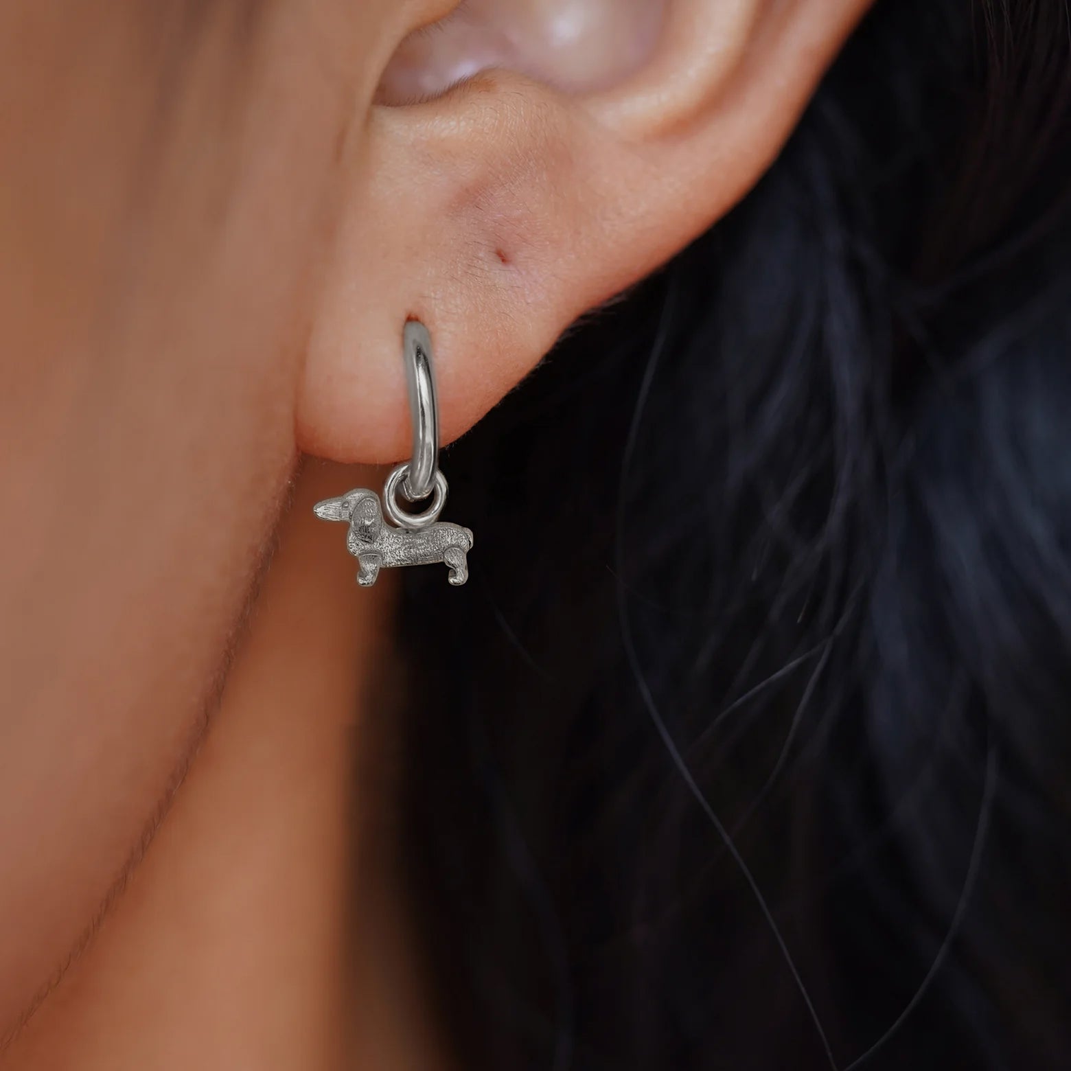 Close up view of a model's ear wearing a white gold dog Charm on a Curvy Huggie