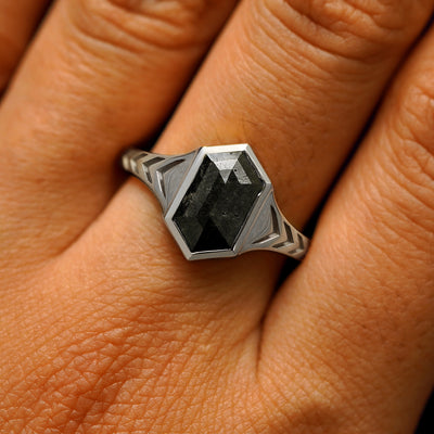 Close up view of a model's fingers wearing a 14k white gold elongated hexagon black diamond engraved chronos ring