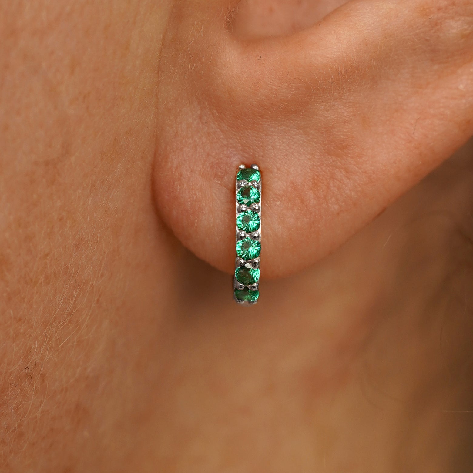 Close up view of a model's ear wearing a white gold Small Emerald Huggie Hoop