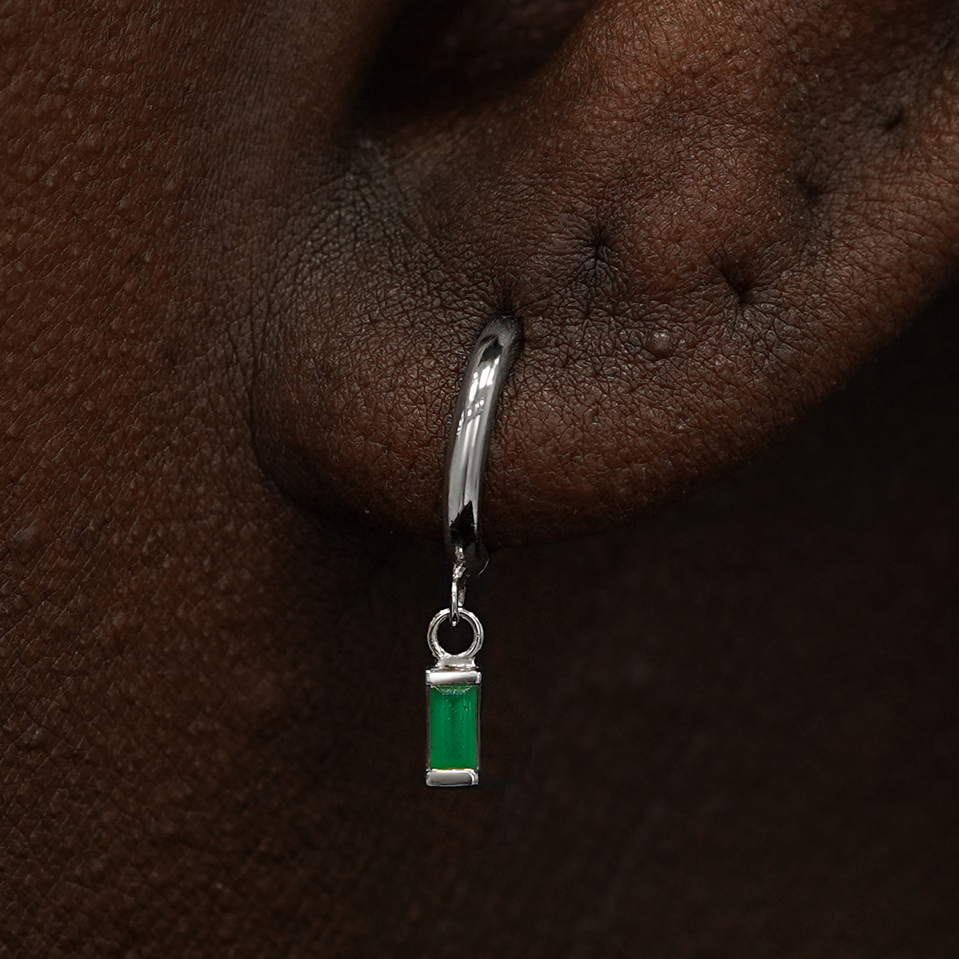 Close up view of a model's ear wearing a white gold Baguette Emerald Dangle Huggie Hoop