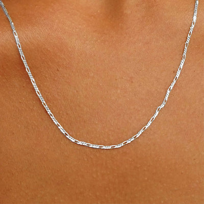 Close up view of a model's neck wearing a solid white gold Figaro Chain