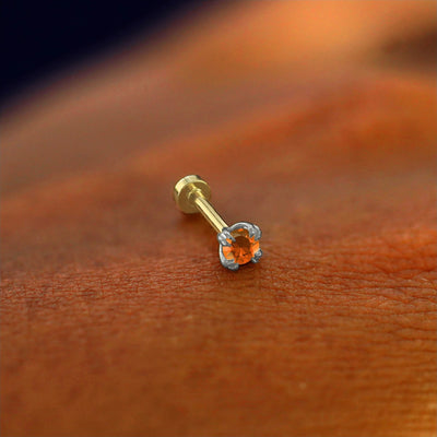 A solid 14k white gold fire opal Piercing resting on the back of a model's hand