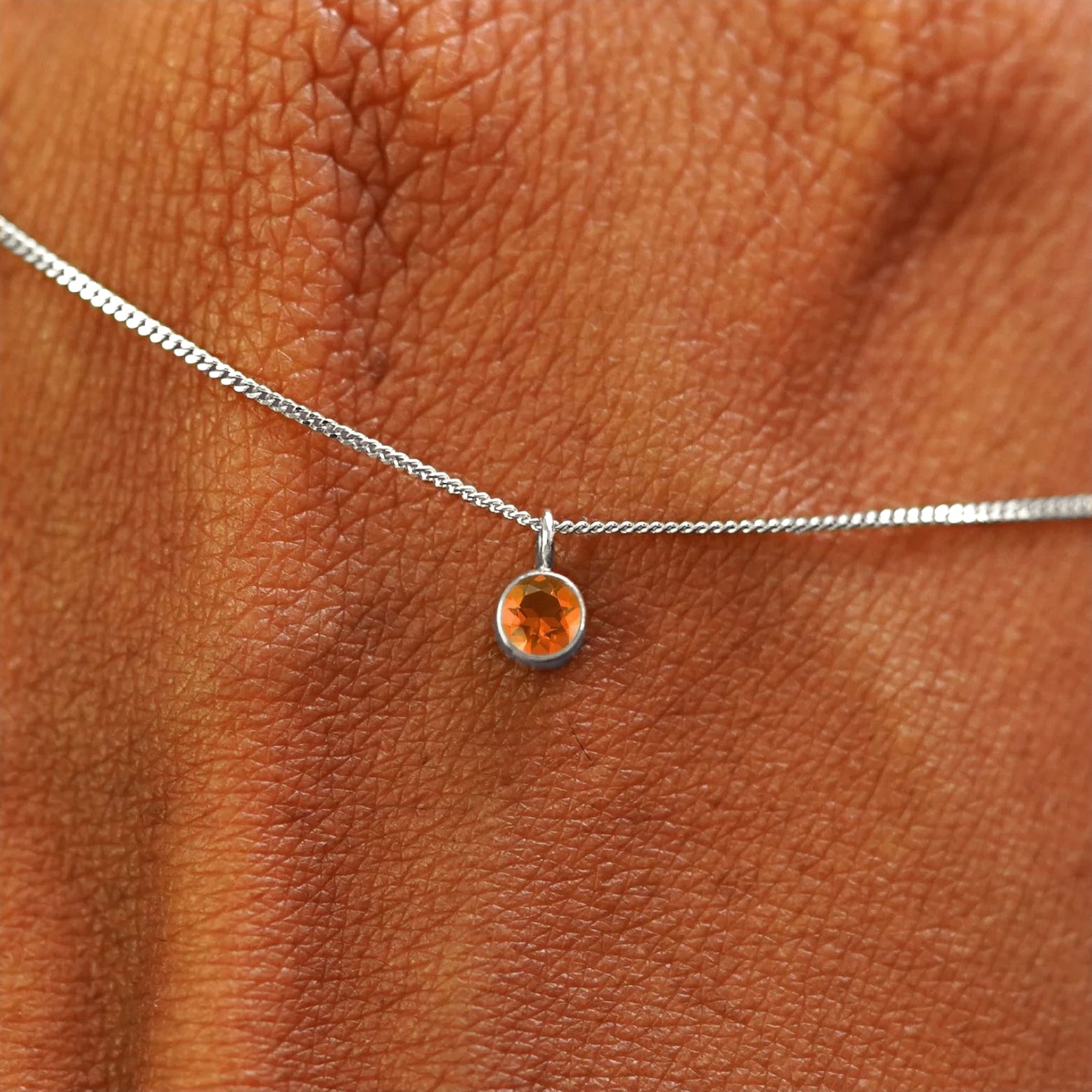 Close up view of a 14k white gold Fire Opal Necklace draped across the back of a model's hand