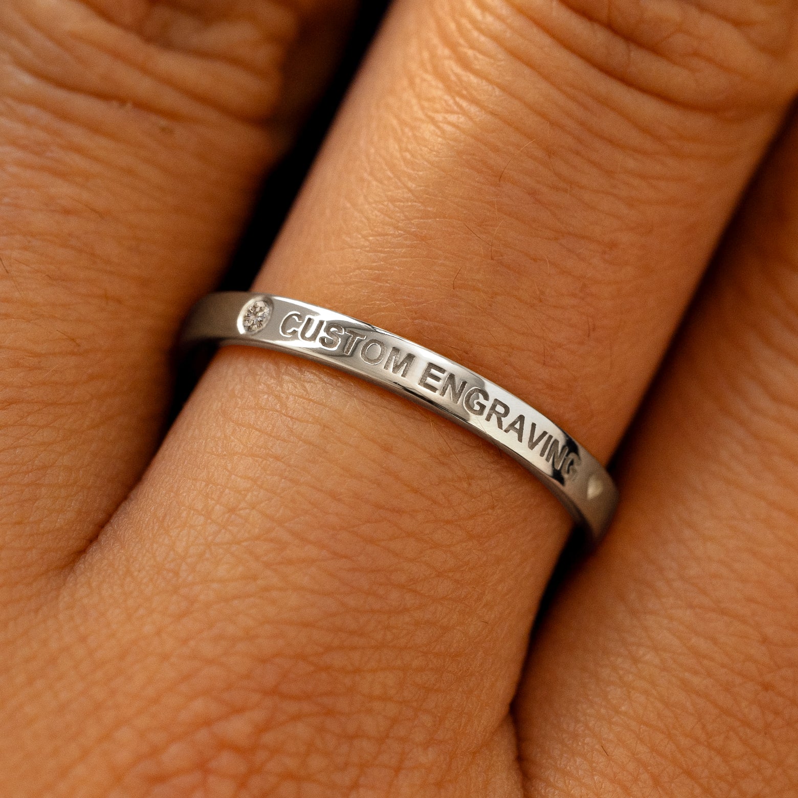 A model's finger wearing a diamond white gold flush gemstone industrial band the words custom engraving on the top