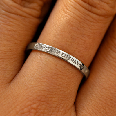 A model's finger wearing a diamond white gold flush gemstone industrial band the words custom engraving on the top