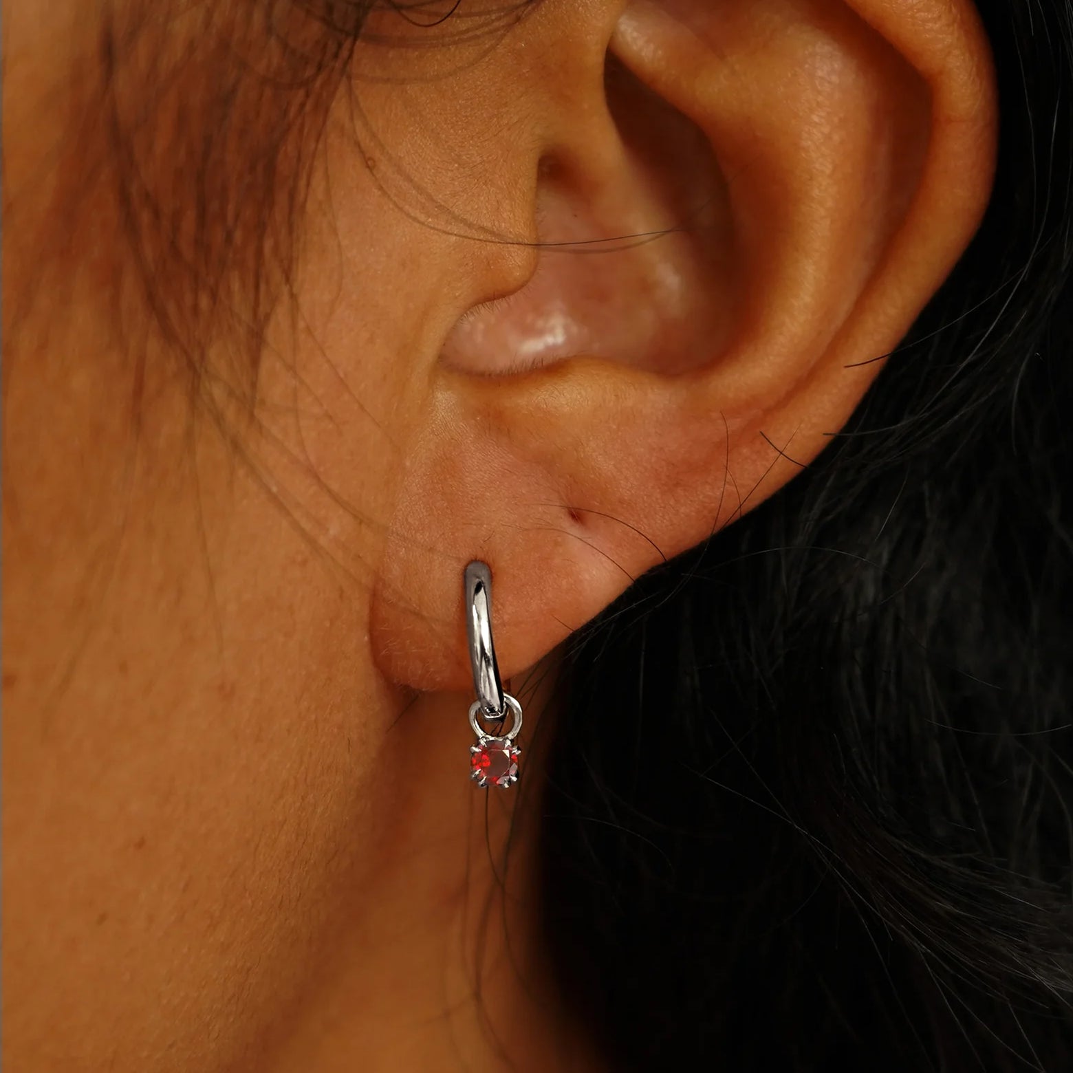 Close up view of a model's ear wearing a white gold Garnet Charm on a Curvy Huggie Hoop