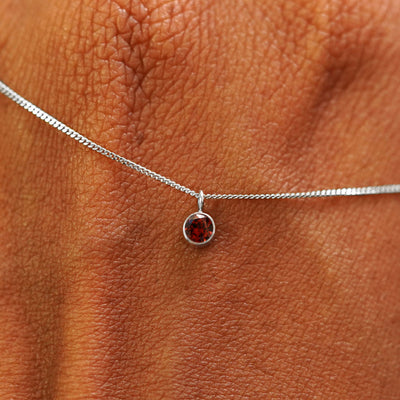 Close up view of a 14k white gold Garnet Necklace draped across the back of a model's hand