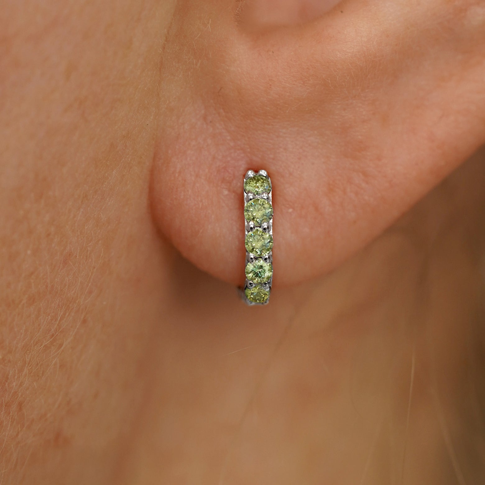 Close up view of a model's ear wearing a white gold Mini Light Green Lab Diamond Huggie Hoop