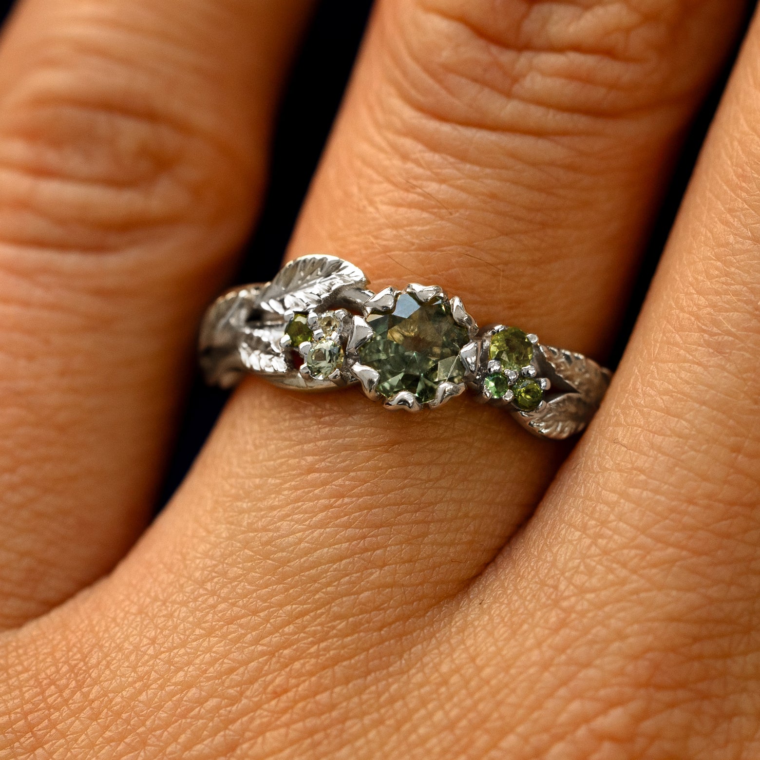 Close up view of a model's fingers wearing a 950 platinum Green Sapphire Leaves and Vines Ring
