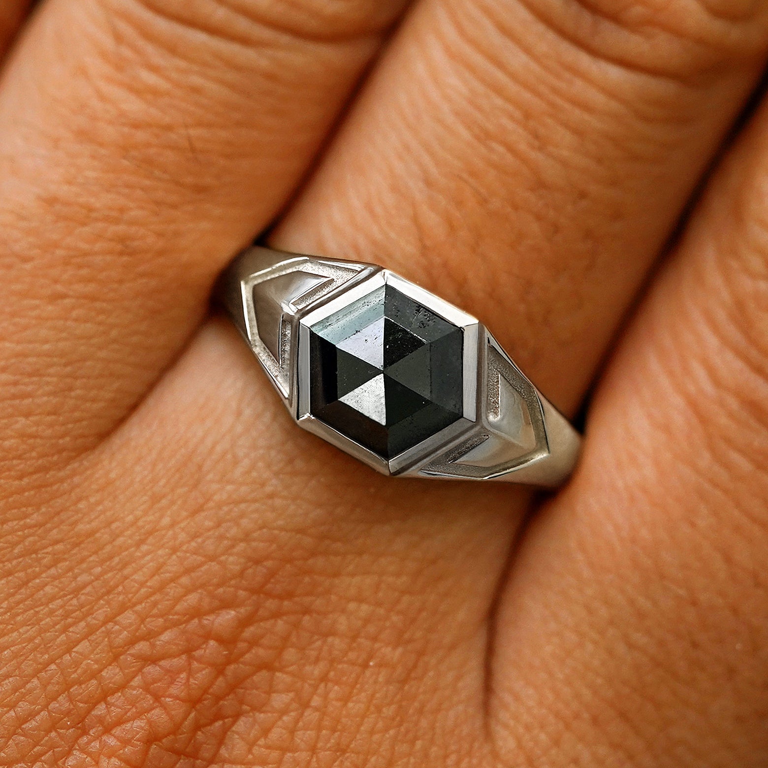 Close up view of a model's fingers wearing a 14k white gold hexagon black diamond engraved transformation ring