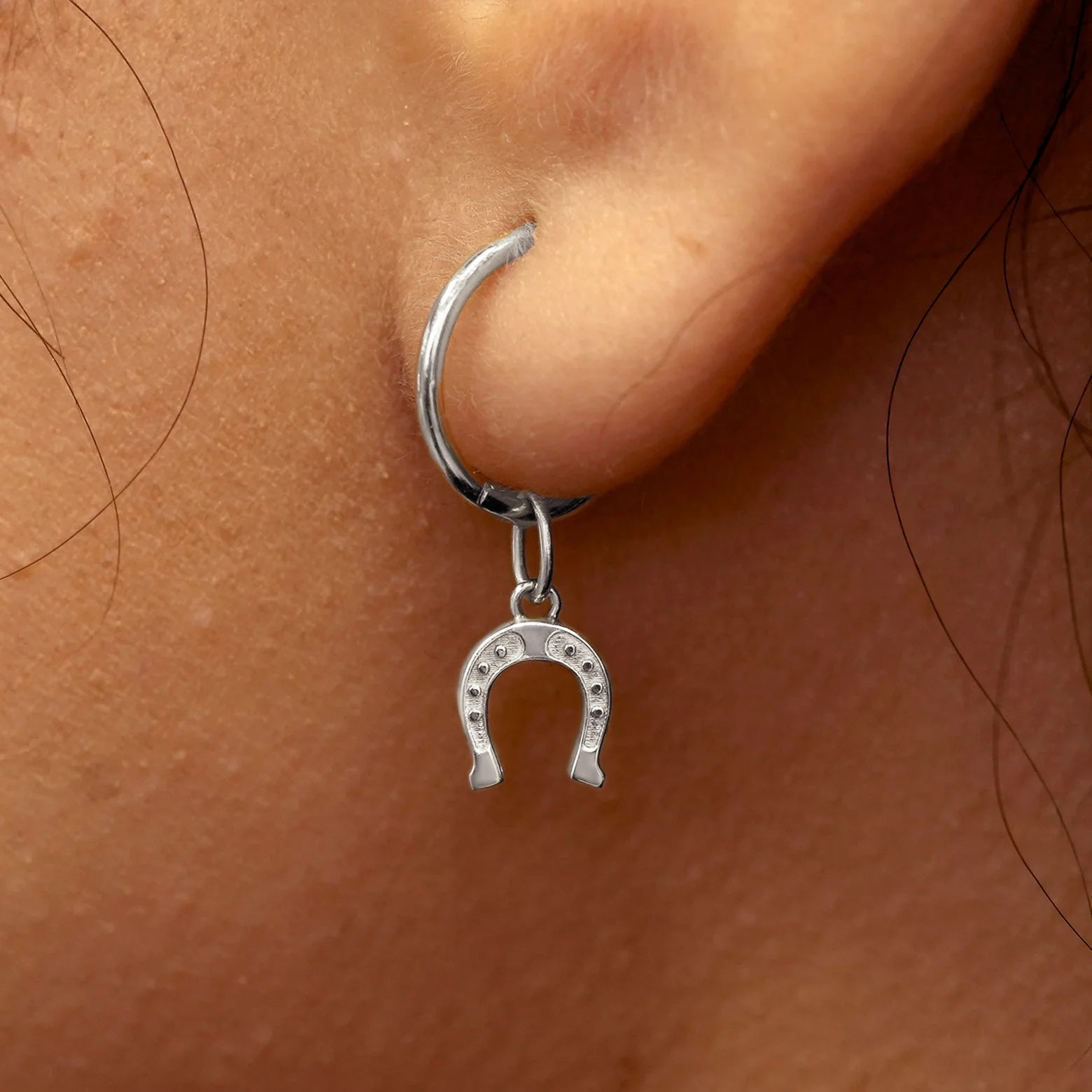 Close up view of a model's ear wearing a white gold Horseshoe Charm on a Small Seamless Huggie Hoop