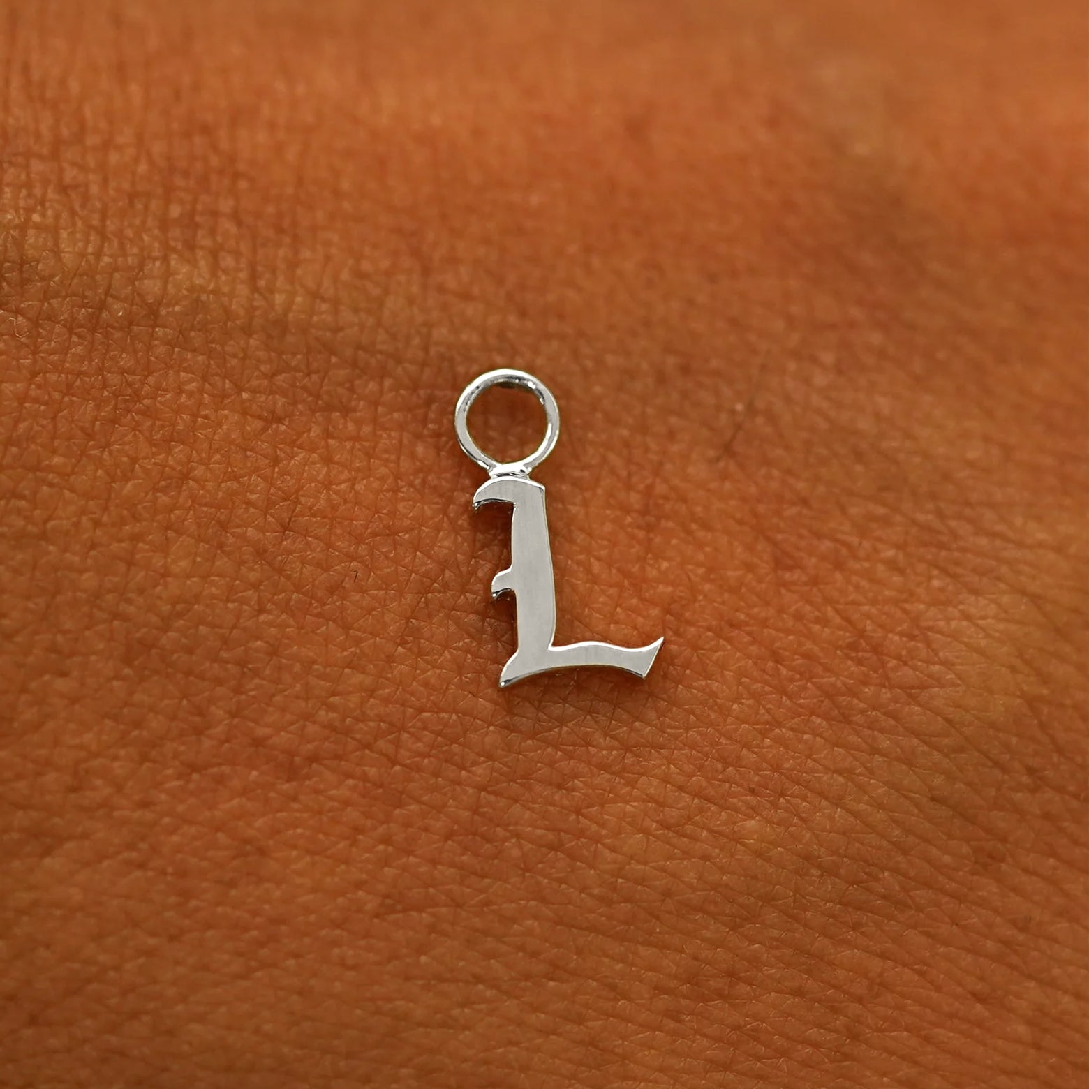 A solid 14k gold Initial Charm for earring in the letter L laying on the back of a model's hand