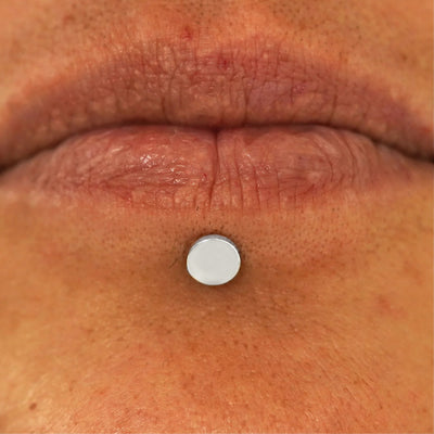 Close up view of a model's lips wearing a 14k white gold Large Circle Flatback in a labret piercing