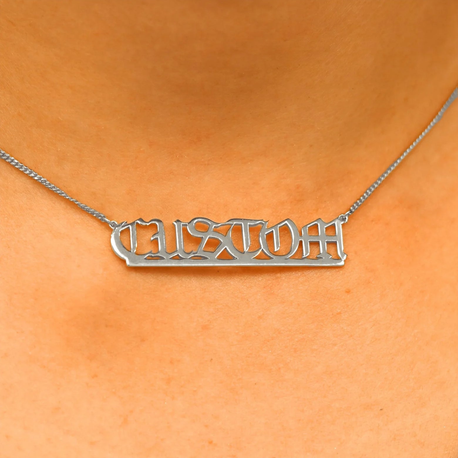 Close up view of a model's neck wearing a Large Custom Nameplate necklace that reads the word Custom