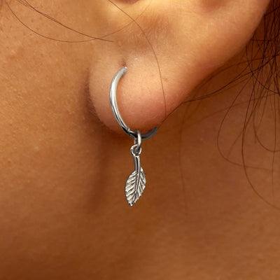 Close up view of a model's ear wearing a white gold Leaf Charm on a Small Seamless Huggie Hoop