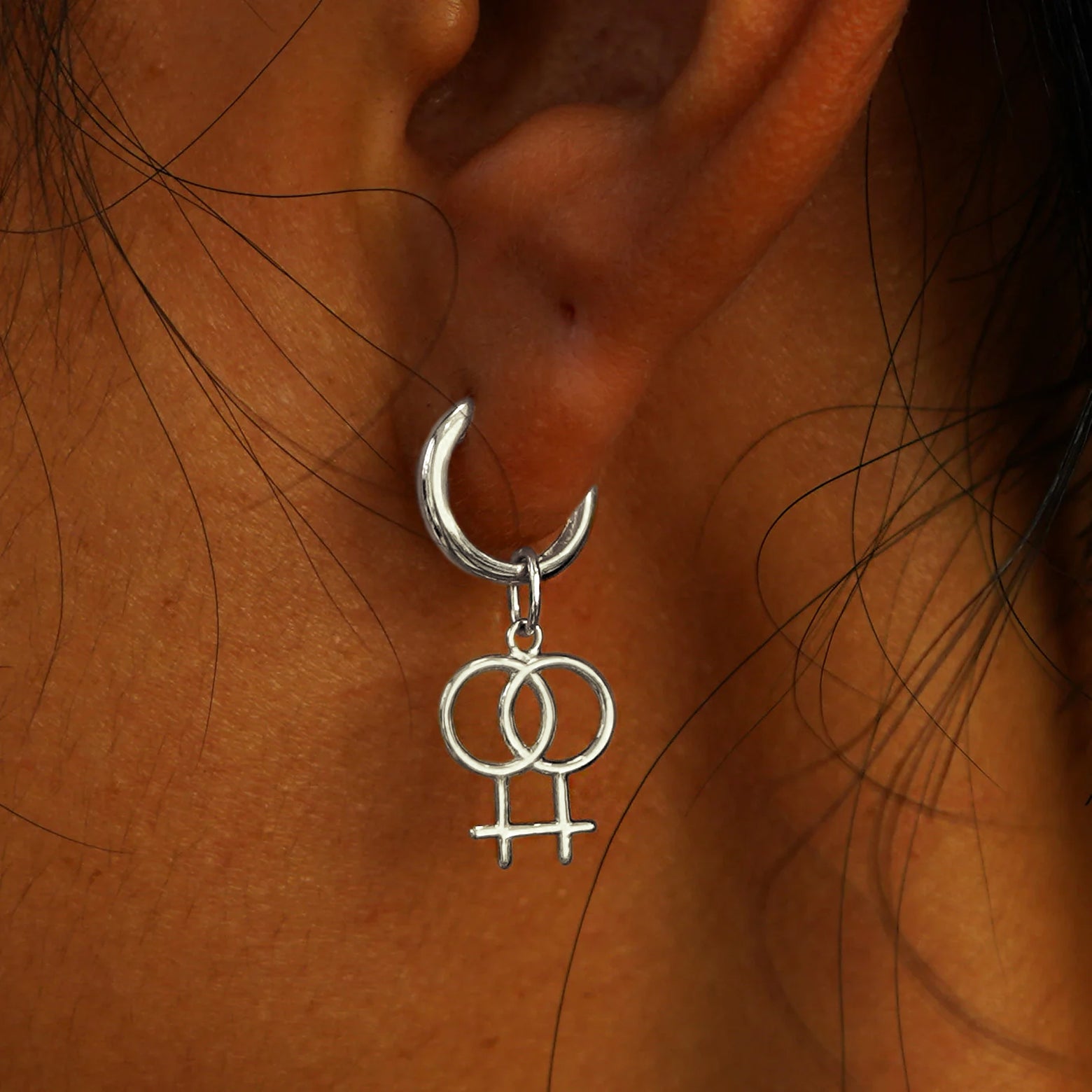 Close up view of a model's ear wearing a white gold Lesbian Symbol Charm on a Curvy Huggie Hoop