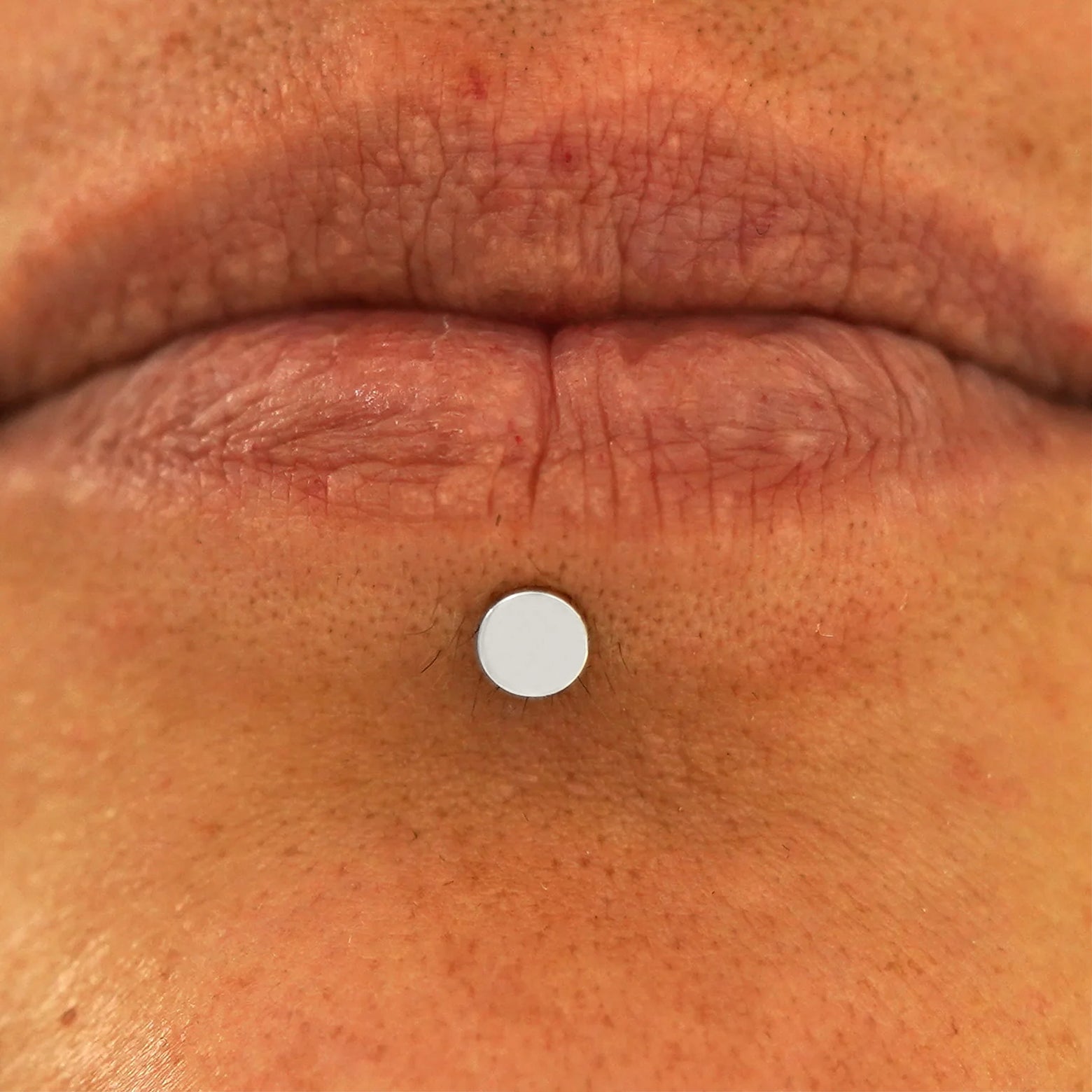 Close up view of a model's lips wearing a 14k white gold Medium Circle Flatback in a labret piercing