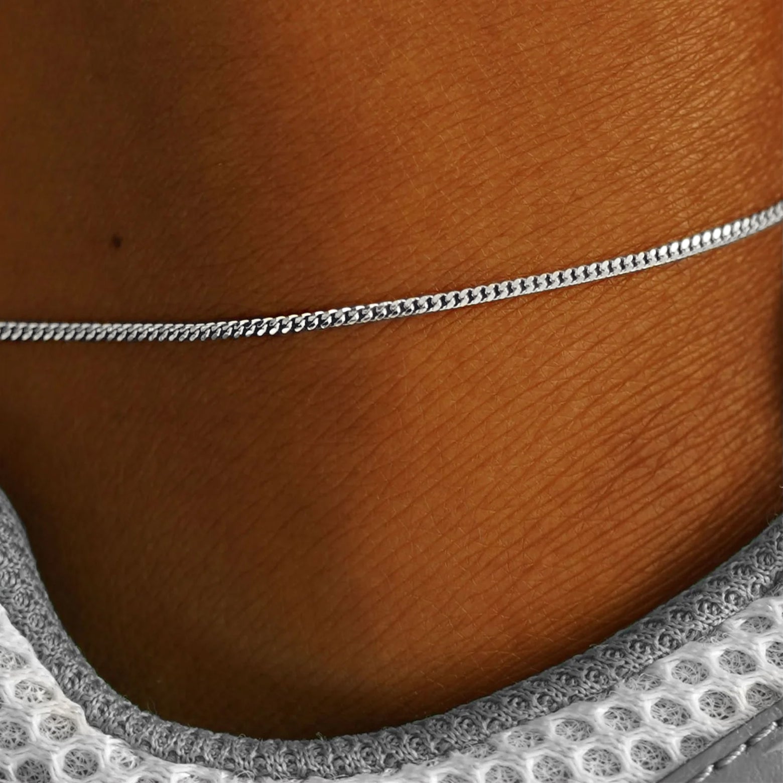 Close up view of a model's ankle wearing a solid white gold Mini Miami Anklet