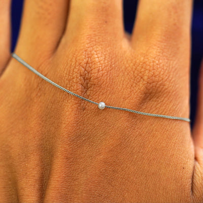 A white gold 2mm pearl slide bracelet resting on the back of a model's hand