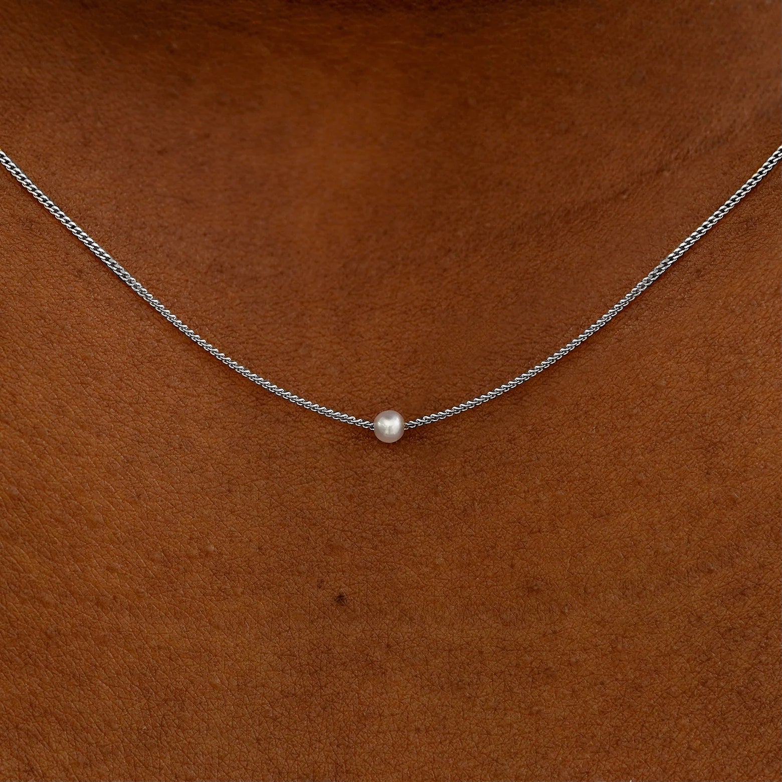 Close up view of a model's neck wearing a white gold Pearl Slide Necklace with a 2mm pearl