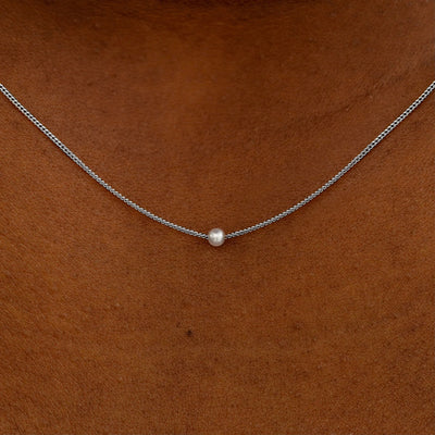 Close up view of a model's neck wearing a white gold Pearl Slide Necklace with a 2mm pearl