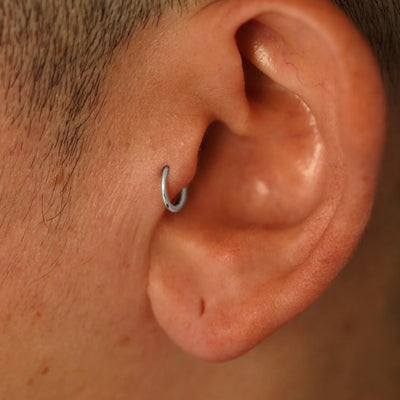 A model's ear wearing a 14k white gold Mini Seamless Huggie Hoop in a tragus piercing