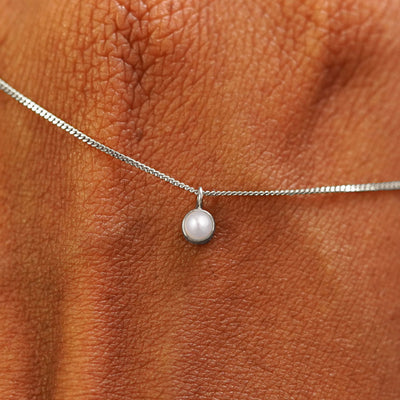 A solid white gold Pearl Necklace draped across the back of a model's hand