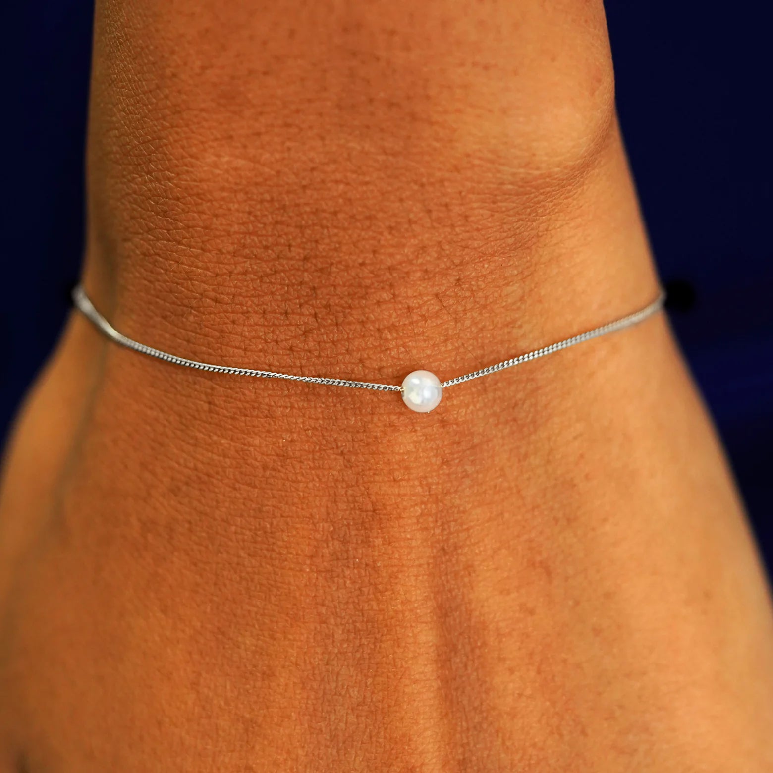 A model's wrist wearing a white gold Pearl Slide Bracelet with a 4mm pearl