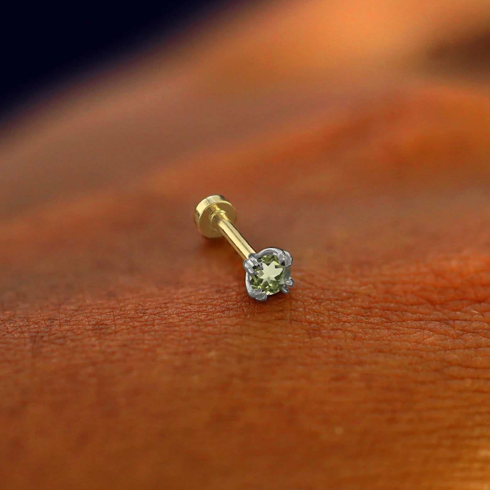 A solid 14k white gold Peridot Flatback Piercing resting on the back of a model's hand