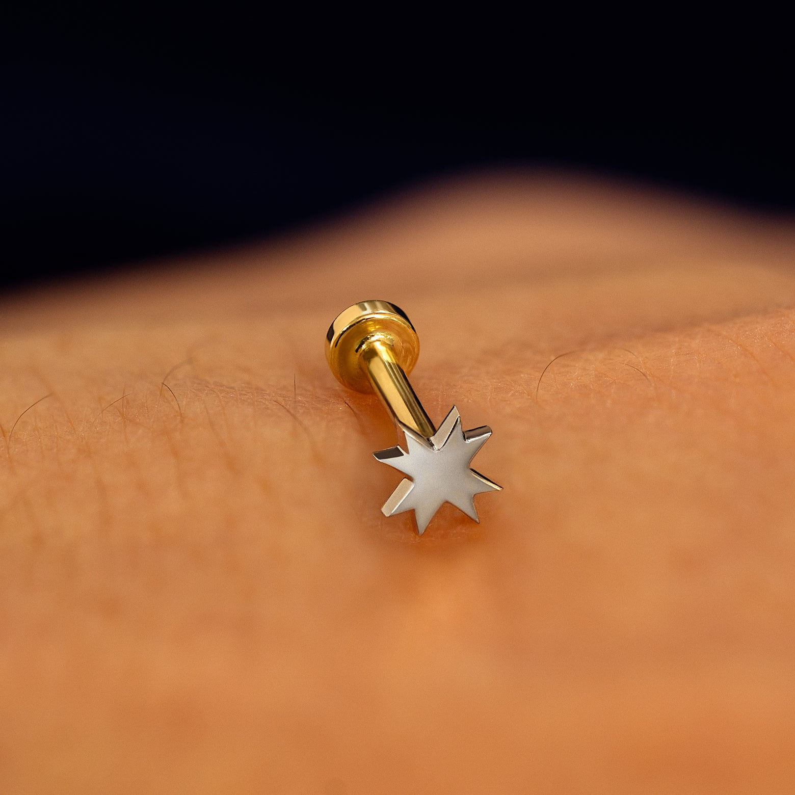 A white gold 8 pointed star flatback piercing with yellow gold backing on a models hand