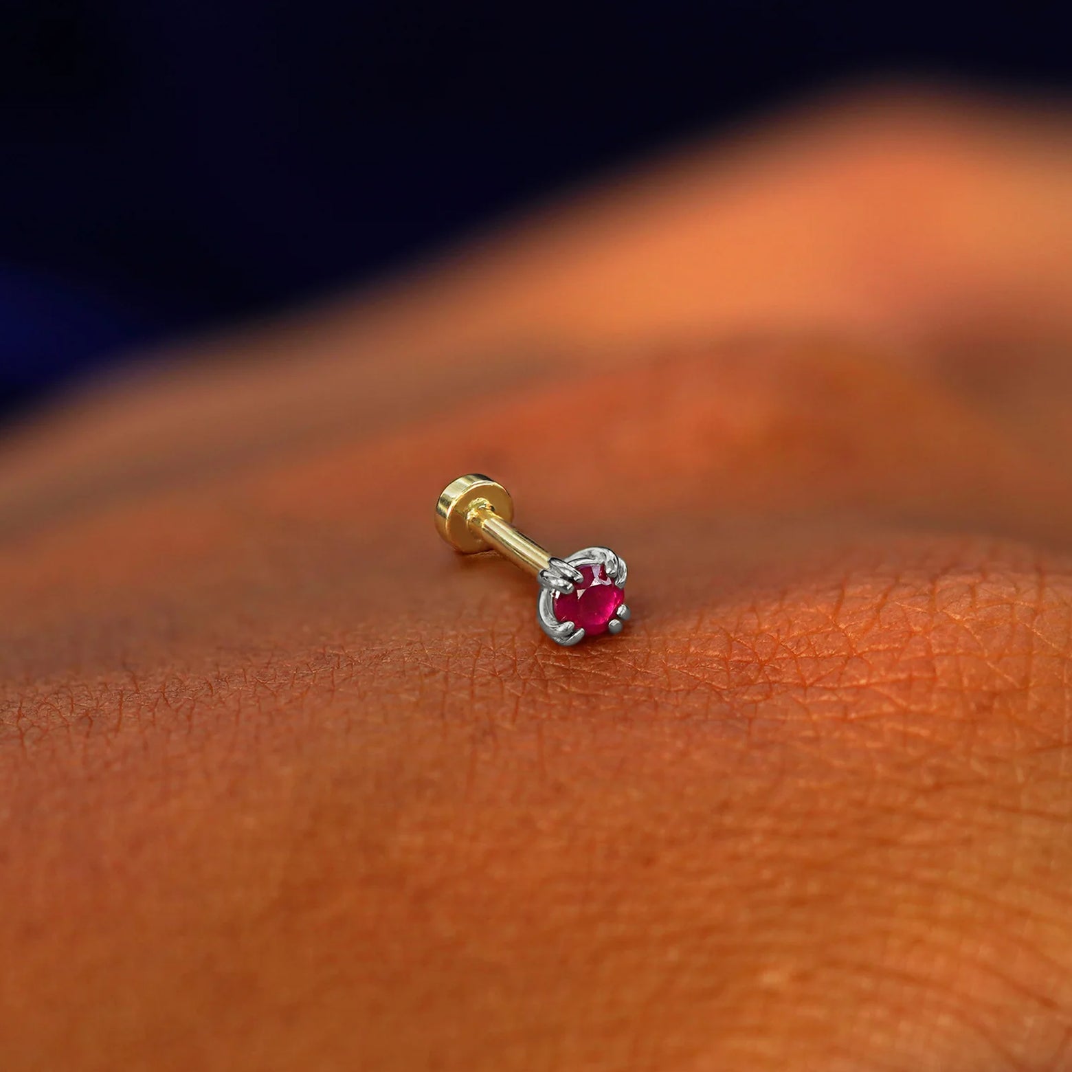 A solid 14k white gold Ruby Flatback Piercing resting on the back of a model's hand
