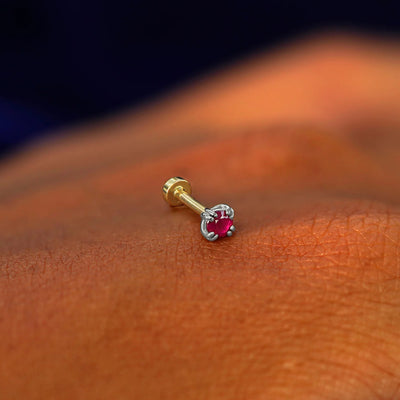 A solid 14k white gold Ruby Flatback Piercing resting on the back of a model's hand