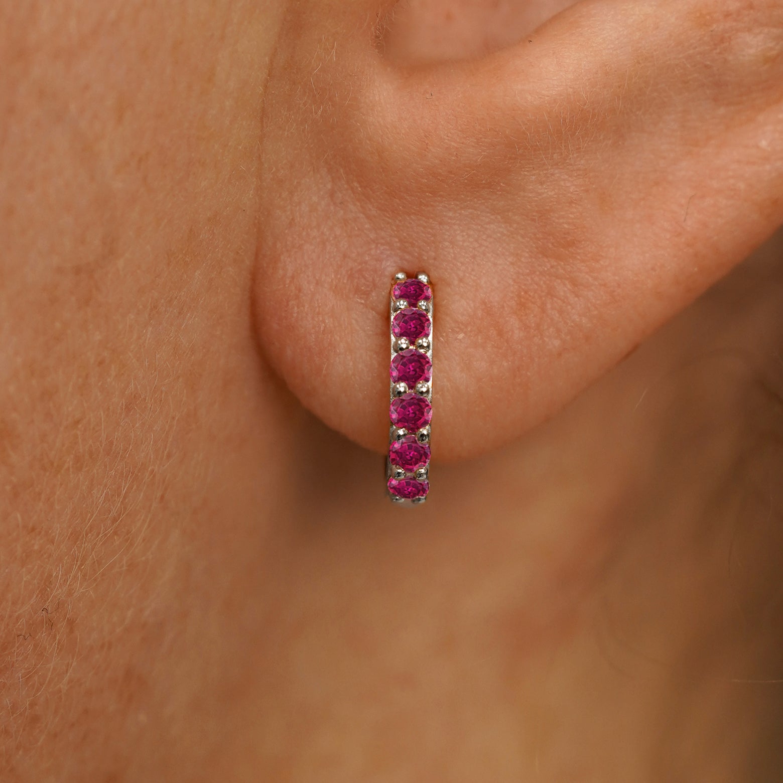 Close up view of a model's ear wearing a white gold Small Ruby Huggie Hoop