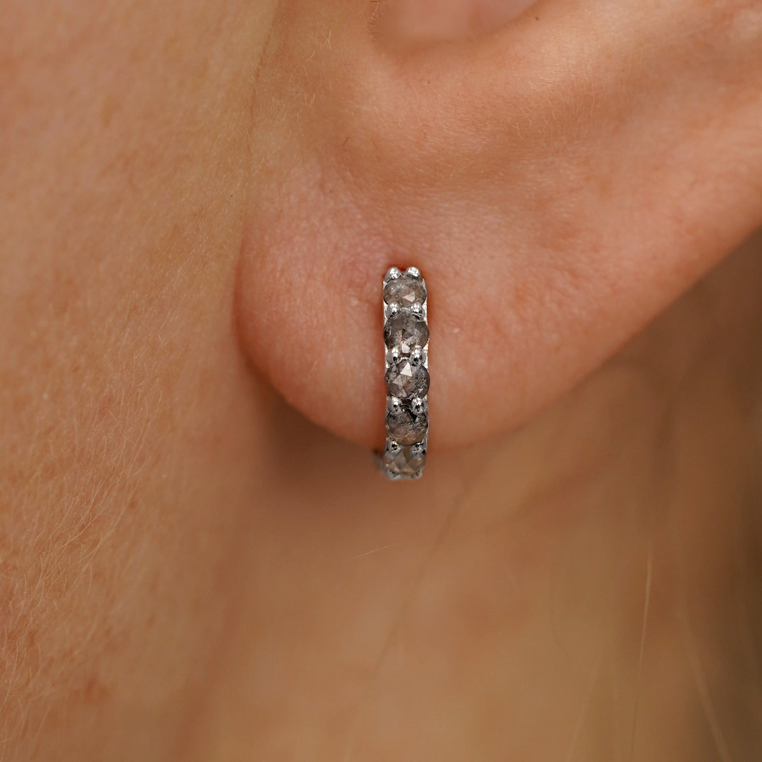 Close up view of a model's ear wearing a white gold Mini Salt and Pepper Diamond Huggie Hoop