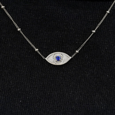 Close up view of a solid 14k white gold sapphire evil eye necklace against a model's black shirt