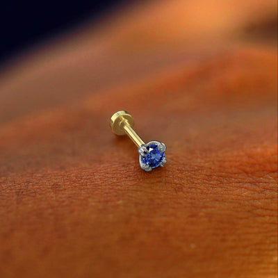 A solid 14k white gold Sapphire Flatback Piercing resting on the back of a model's hand