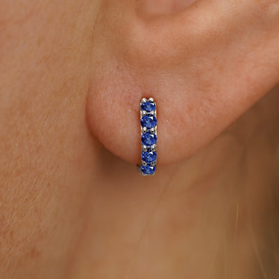 Close up view of a model's ear wearing a white gold Mini Blue Sapphire Huggie Hoop