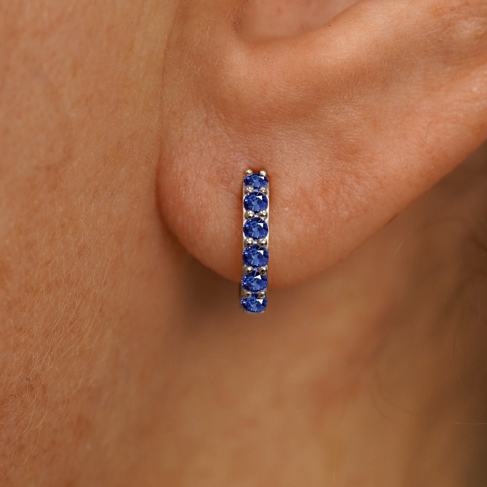 Close up view of a model's ear wearing a white gold Small Blue Sapphire Huggie Hoop