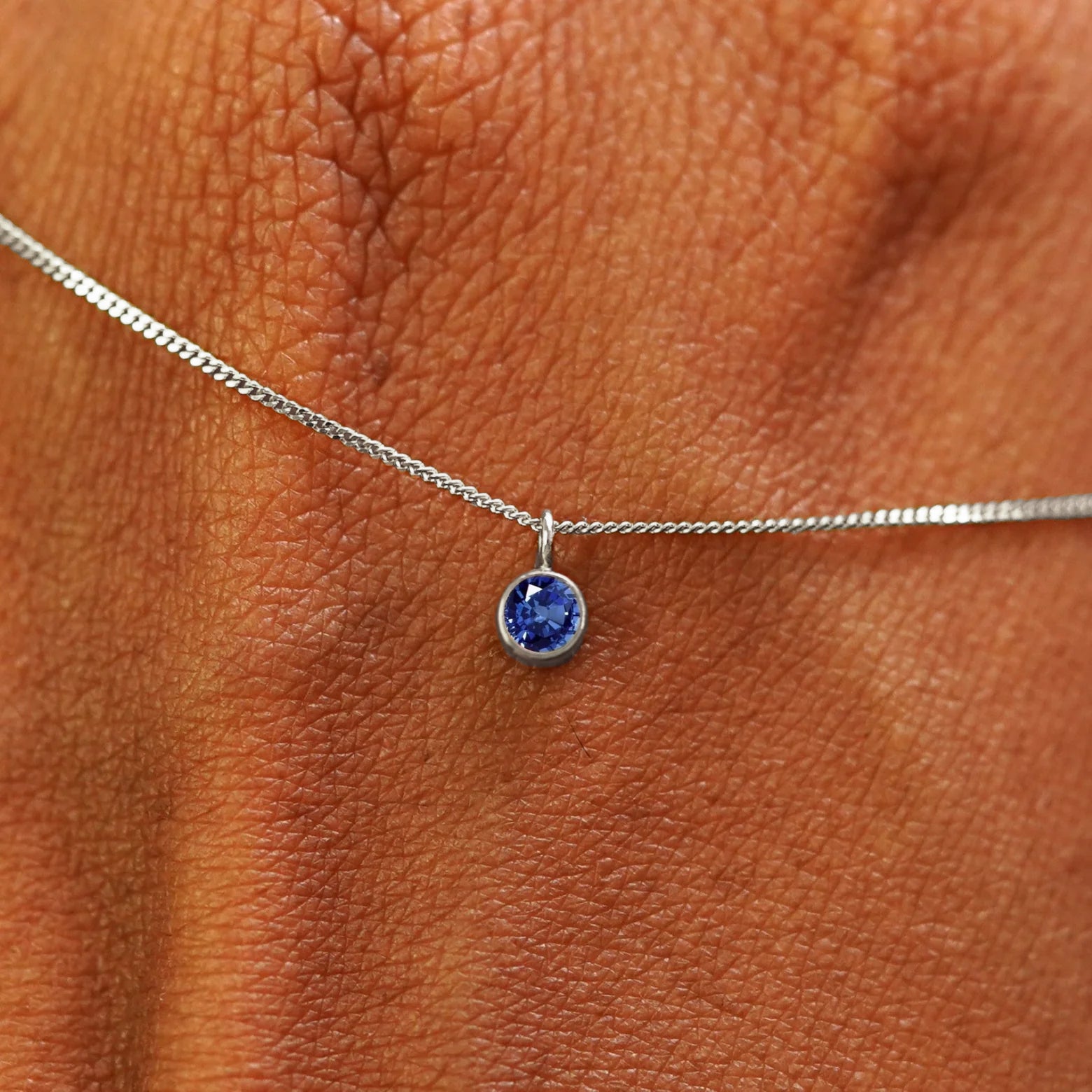Close up view of a 14k white gold Sapphire Necklace draped across the back of a model's hand