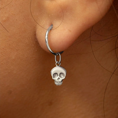 Close up view of a model's ear wearing a white gold Skull Charm on a Small Seamless Huggie Hoop