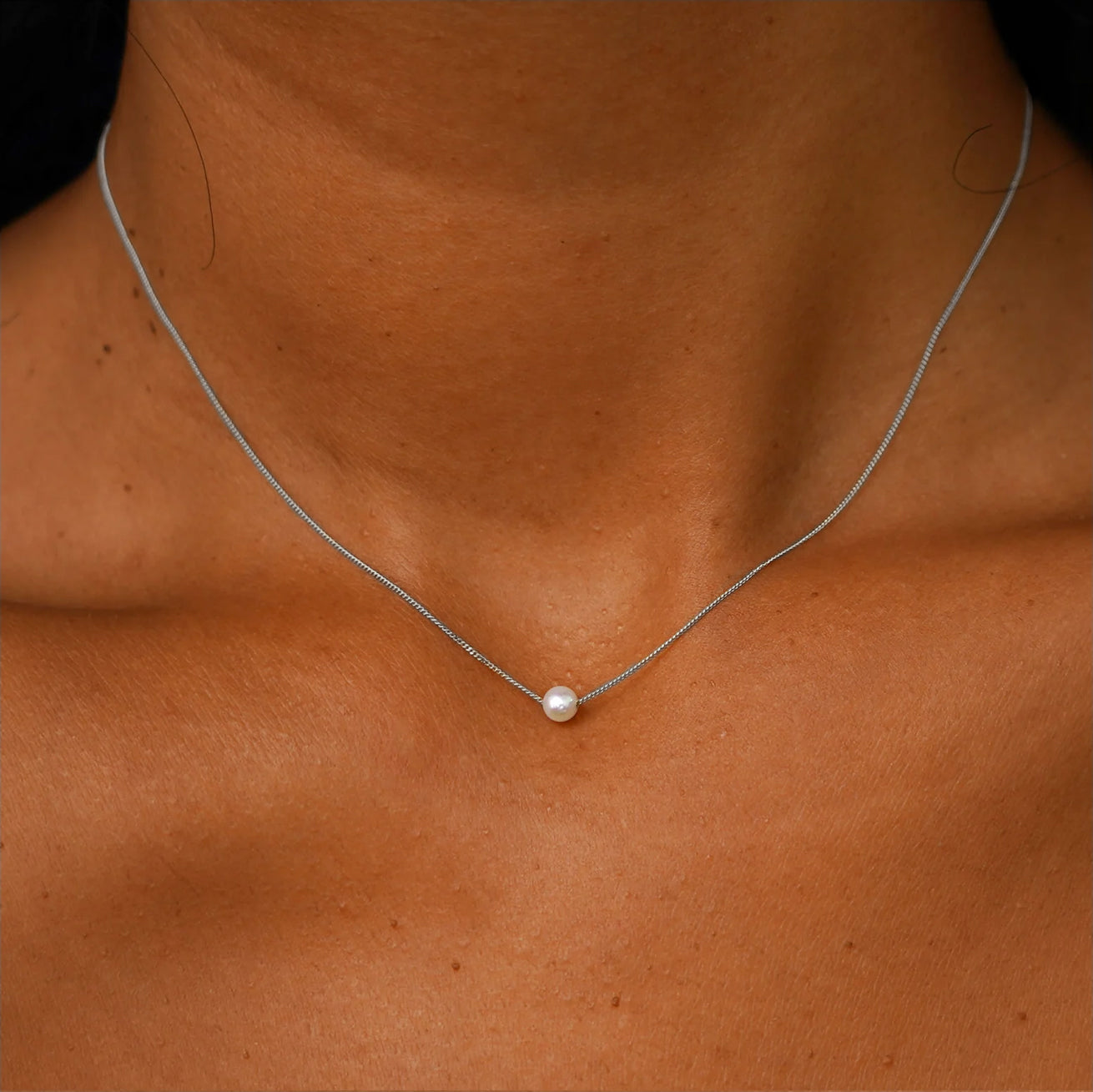 A model's neck wearing a white gold Pearl Slide Necklace with a 4mm pear