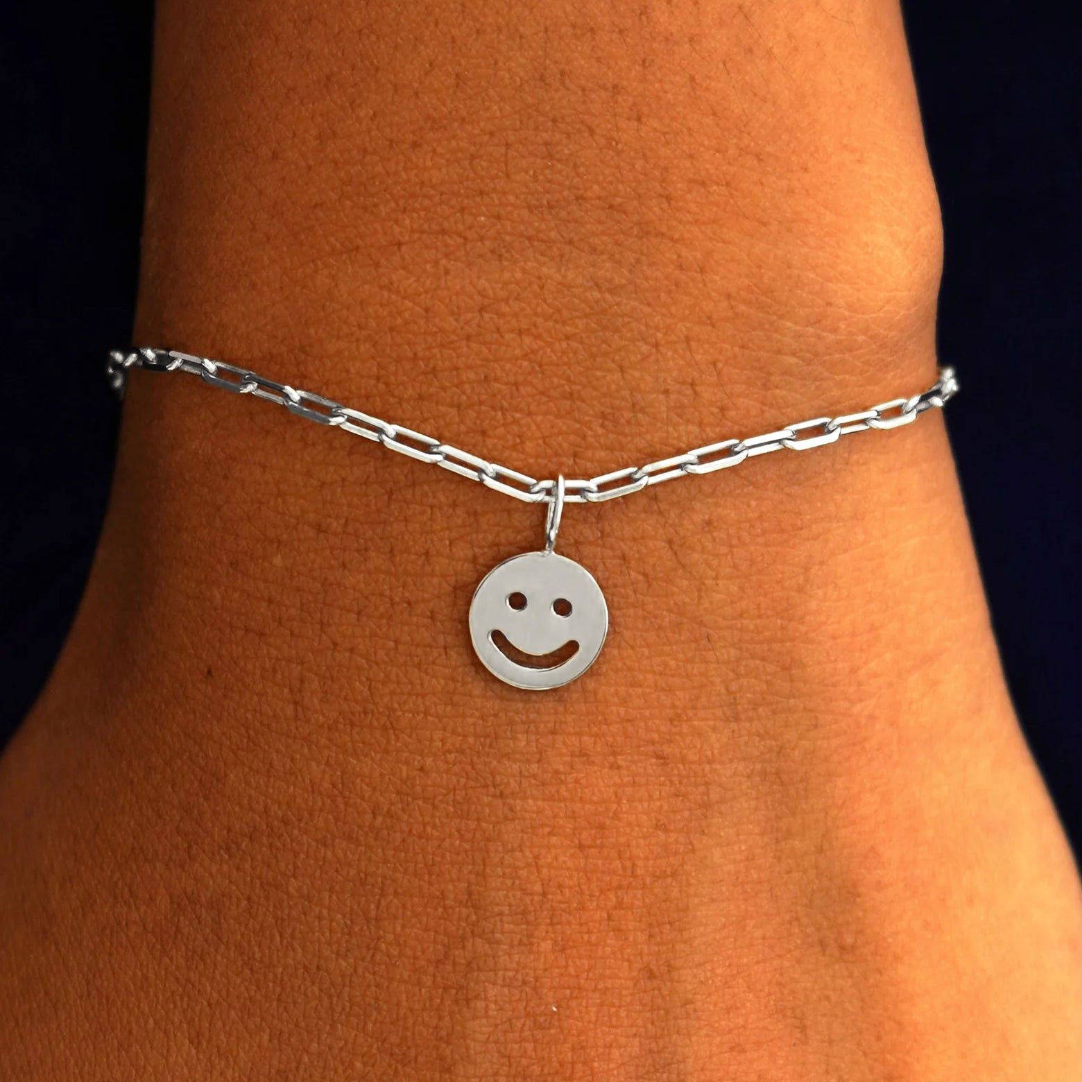 Close up view of a model's wrist wearing a white gold Smiley Face Charm on a Butch Chain Bracelet