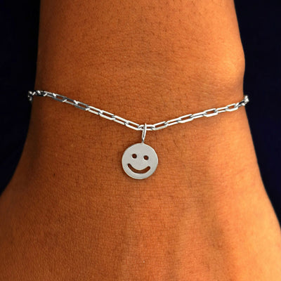 Close up view of a model's wrist wearing a white gold Smiley Face Charm on a Butch Chain Bracelet