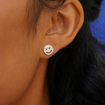 Close up view of a model's ear wearing a white gold Smiley Face Earring