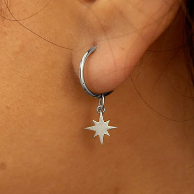 Close up view of a model's ear wearing a white gold Starburst Charm on a Small Seamless Huggie Hoop